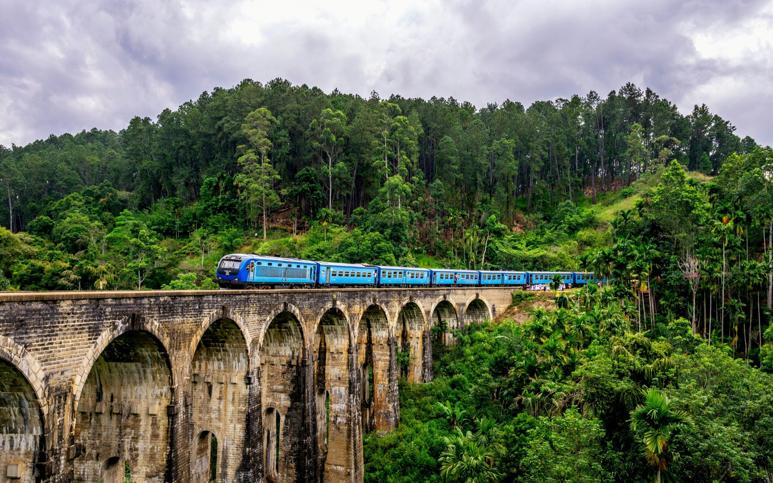 The famous blue train crossing the Nine Arch Bridge in Ella, Sri Lanka, surrounded by mountains.
